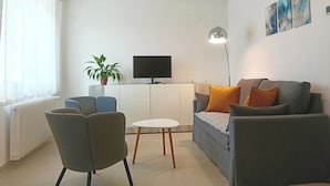 Un salon moderne avec un canapé, des fauteuils, un téléviseur, une plante et des œuvres d’art accrochées au mur.