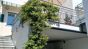 Un bâtiment avec un escalier, un balcon agrémenté d’un parasol beige et un arbre aux feuilles vertes.