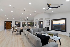A spacious living room with a large grey sectional sofa, a dining area with a wooden table and chairs, and a ceiling fan.
