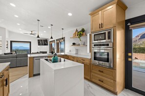 A modern kitchen with a central island, stainless steel appliances, wooden cabinets, and a large window with a mountain view.