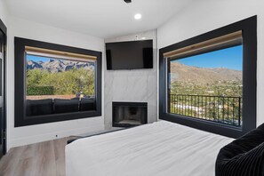 Une chambre à coucher avec un lit, une cheminée, une télévision et de grandes fenêtres offrant une vue sur les montagnes.