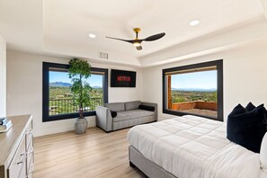Un dormitorio con cama, sofá gris, planta en maceta y televisor de pared mostrando 'NETFLIX'.