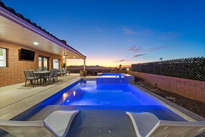 Una piscina con zona de patio, un muro de ladrillo y vistas a la montaña al atardecer.
