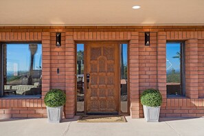 Un edificio de ladrillo con una puerta de madera grande, dos macetas y una vista despejada del exterior.