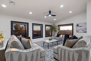Una sala de estar moderna con un conjunto de sofás, una mesa de centro y ventanas amplias que dan a vistas del exterior.