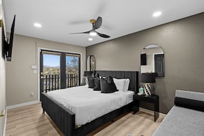 Un dormitorio con cama, mesita de noche, espejo, ventilador de techo y vistas por una puerta.