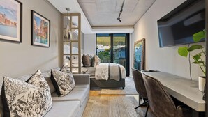 A modern bedroom with a bed, a sofa, a desk, and a TV. - Luxury Living @ Station House | No loadshedding (Cape Town)