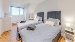 A modern bedroom with two beds, a white dresser, a nightstand, and a window. - The Bunker - UK47763 (Bamburgh)