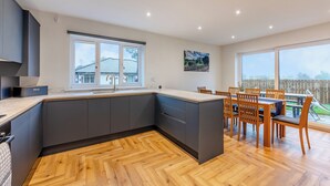 A modern kitchen with a large island, dark cabinetry, and a dining area with wooden chairs and a table. - The Bunker - UK47763 (Bamburgh)