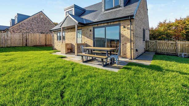 A single-story house with a patio, a large sliding glass door, and a small attached garage. - The Bunker - UK47763 (Bamburgh)