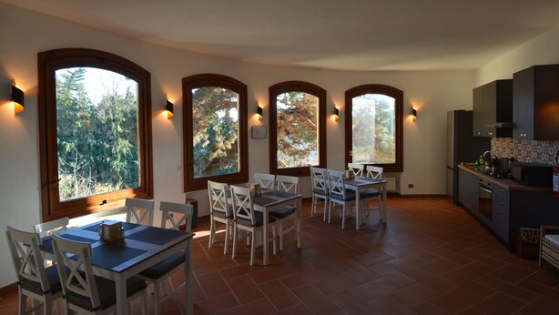Un comedor con mesa y sillas, ventanas grandes con arcos y una zona de cocina con armarios y electrodomésticos.