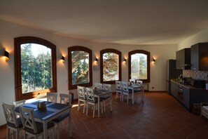 Un espace repas comprenant une table et des chaises, de grandes fenêtres à arc en plein cintre, et un coin cuisine avec des placards et des appareils électroménagers.