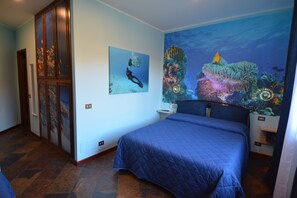 Un dormitori amb un llit gran, un mural a la paret que representa una escena submarina i una porta amb un panell de vidre.