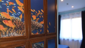 Una habitación con una gran pared de acuario, una cama con colcha azul y una ventana con cortinas.