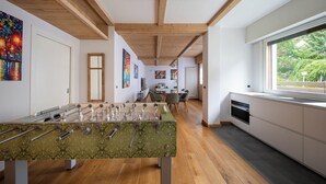 A modern kitchen with wooden beams, a foosball table, and a large window overlooking greenery. - Santa Barbara 31 - Three Bedroom Apartment, Sleeps 7 (Bormio)