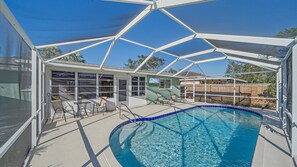 A covered outdoor swimming pool with a clear blue water feature, surrounded by a white roof structure, and a wooden fence in the background.