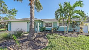 A single-story house with a garage, surrounded by a well-maintained lawn and palm trees.