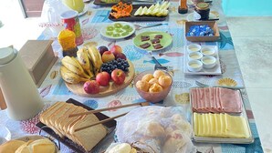 A table with various food items and drinks, including fruits, sandwiches, and pastries. - Pousada Américas (Guarujá)