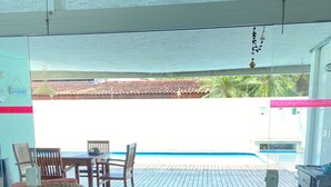 A covered outdoor area with a wooden deck, wicker chairs, and a table. - Pousada Américas (Guarujá)