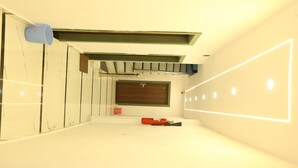 Una habitación moderna y luminosa con un espejo grande, una puerta de madera y un objeto rojo en el suelo.