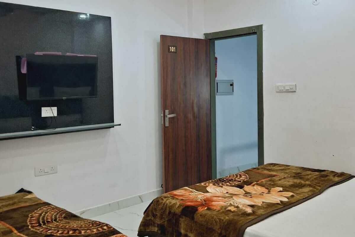 Un dormitorio con dos camas, un ventilador de techo, un televisor montado en la pared y una puerta con el símbolo del número.