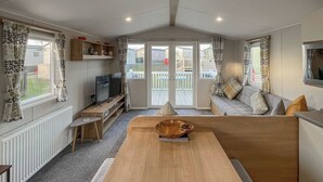 A cozy living room with a wooden table, a sofa, a TV, and a balcony with a view. - 2 bedroom accommodation in Heysham, near Morecambe (Heysham, near Morecambe)