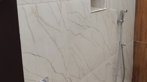 A bathroom with a marble wall, a shower, and a toilet. - Srikrishna Paradise (Tiruvannamalai)