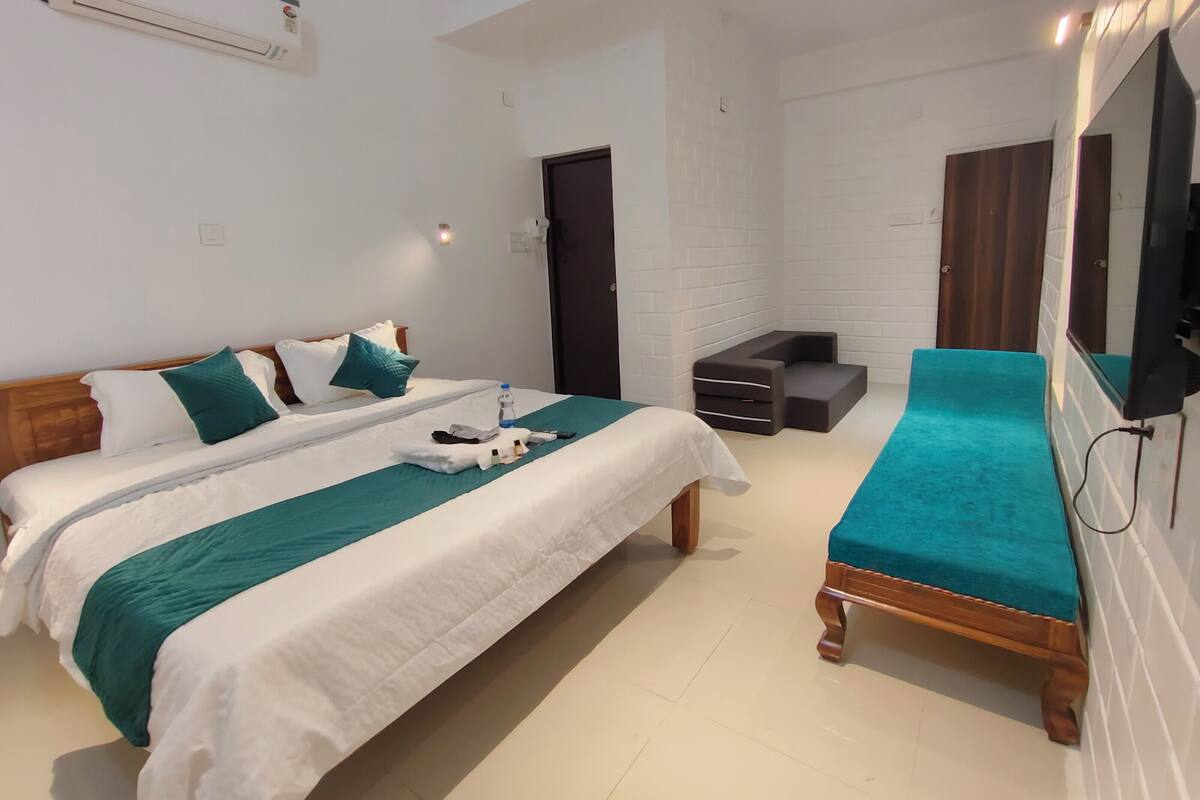 A modern hotel room with a large bed, a small seating area, and a TV mounted on the wall.