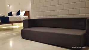A modern bedroom with a bed, a dark-colored sofa, and a white brick wall. - Srikrishna Paradise (Tiruvannamalai)