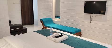 Una habitación de hotel moderna con una cama grande, un sillón azul, un televisor de pantalla plana y un espejo.