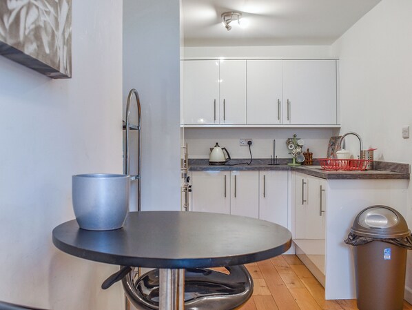 A compact kitchen with white cabinets, a sink, a kettle, and a trash bin.