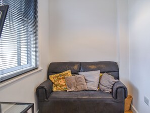 A dark brown leather sofa with multiple cushions against a white wall, positioned next to a window with blinds. - 1 bedroom accommodation in Bournemouth (Bournemouth)