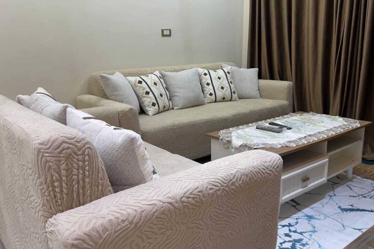 A living room with a beige sofa set, a coffee table, and a patterned rug.