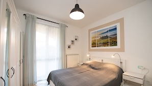 Une chambre à coucher avec un lit, une table de chevet, une lampe, un radiateur et une fenêtre avec des rideaux.