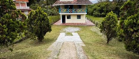 A two-story building with a tiled roof, surrounded by greenery and a paved path leading to the entrance.