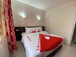 A hotel room with a bed, white curtains, and a red and white bedspread.