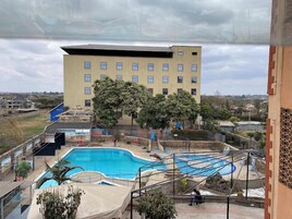 A swimming pool with a slide, surrounded by trees and a building with multiple windows.