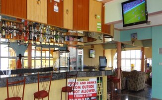 A bar area with a Coca-Cola refrigerator, a television mounted on the wall, and a sign prohibiting outside food and drinks.