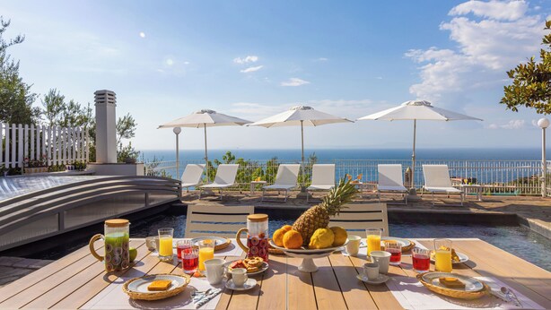 Preparación para el desayuno con una mesa, sillas y sombrillas con vista a una piscina y al océano.