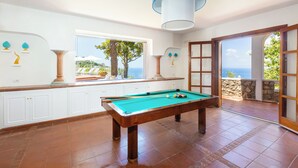 Una mesa de billar en una habitación con armarios blancos y vista al mar.