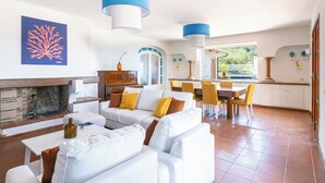 Una sala de estar moderna con chimenea, sofás blancos, sillas amarillas y un comedor con mesa y sillas.