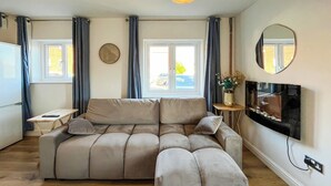 Ein Wohnzimmer mit einer großen L-förmigen Couch, einem flachbildfernseher an der Wand und einem kleinen Beistelltisch.