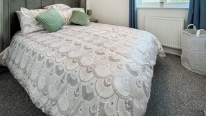 Ein ordentlich bezogenes Bett mit einem gemusterten Überwurf, einem grauen Kopfteil und zwei Kissen.
