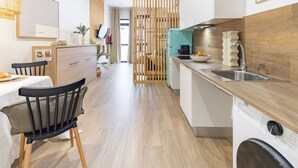 A modern kitchen with wooden flooring, a dining area with a table and chairs, and a washing machine.