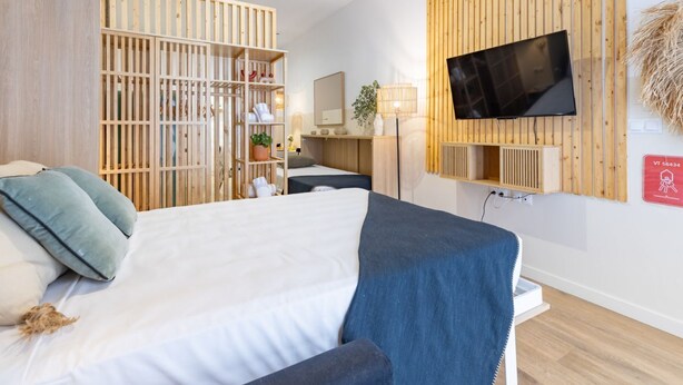 Una camera d'albergo con un letto, una TV fissata al muro, un armadio in legno e una scrivania con una lampada.