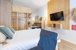 Una habitación de hotel con cama, televisión instalada en la pared, armario de madera y escritorio con lámpara.