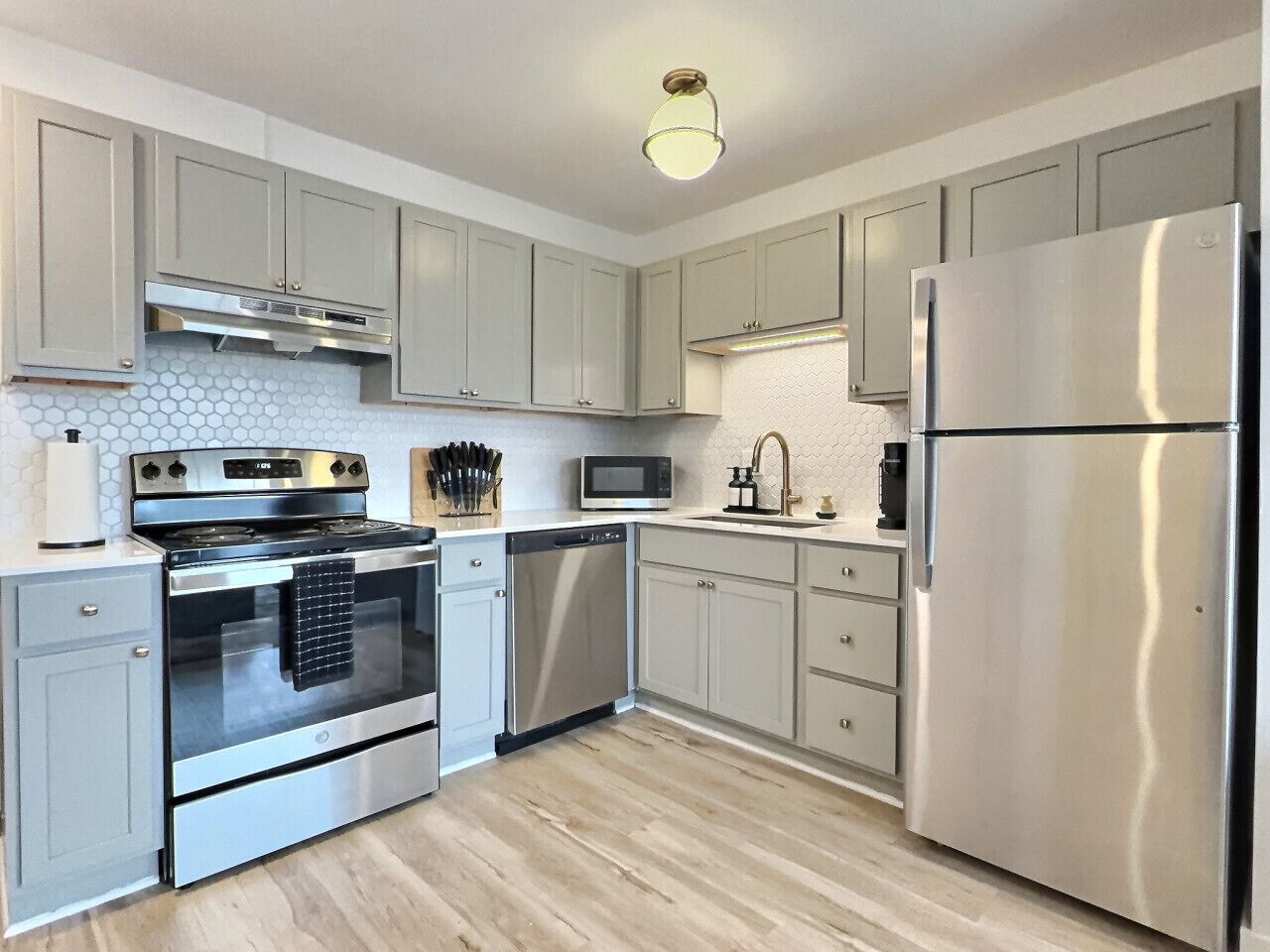 A modern kitchen with light grey cabinets, stainless steel appliances, and a wooden floor.