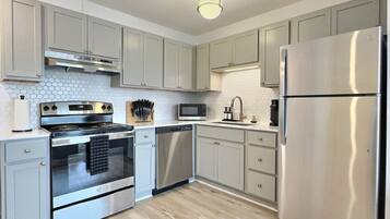 A modern kitchen with light grey cabinets, stainless steel appliances, and a wooden floor.