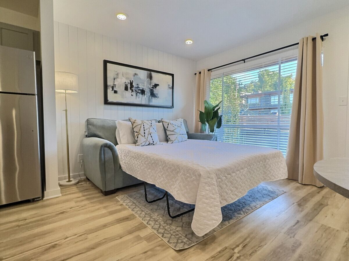 A bedroom with a bed, a sofa, a lamp, and a window with curtains.