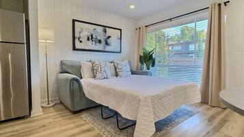 A bedroom with a bed, a sofa, a lamp, and a window with curtains.